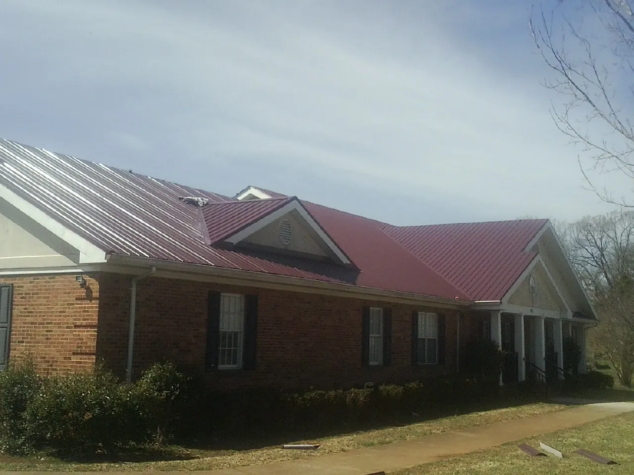Red metal roof with gabled entries on a long brick building, from a Hail Damage Roof Repair job in Reed Point