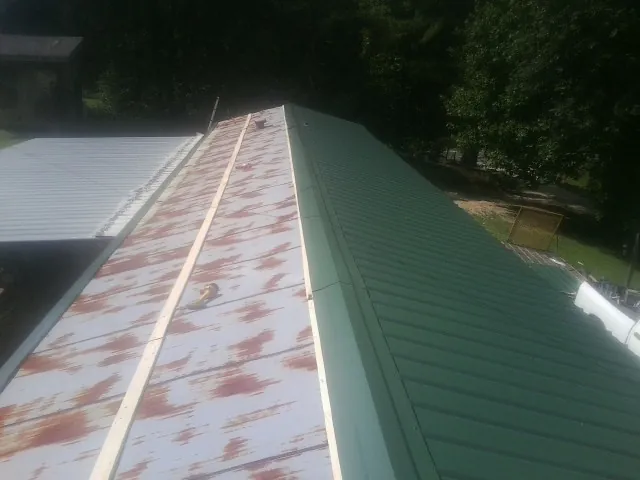 Old rusted panels beside newly installed green metal roofing — Wind Damage Roof Repair by Roofing Brothers in Reed Point