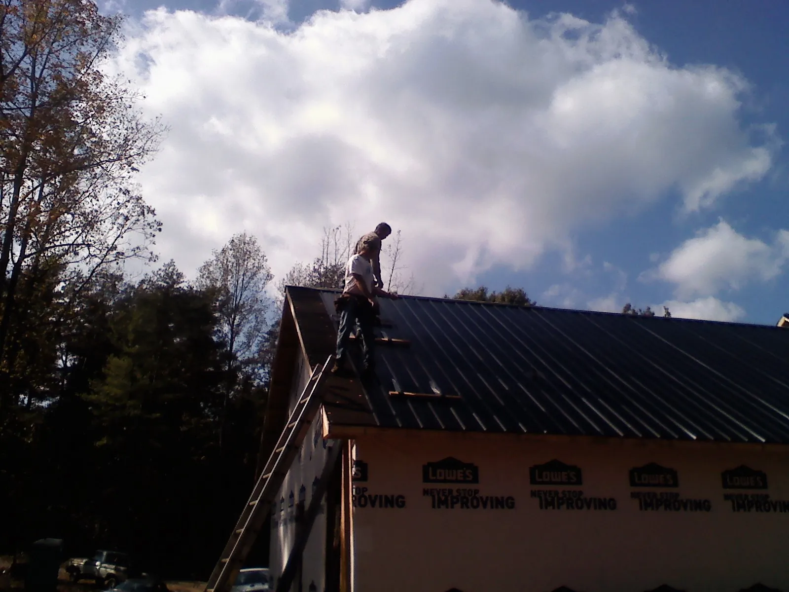 Roofer fastening dark metal panels high against a cloudy sky, from a Roof Inspection job in Reed Point