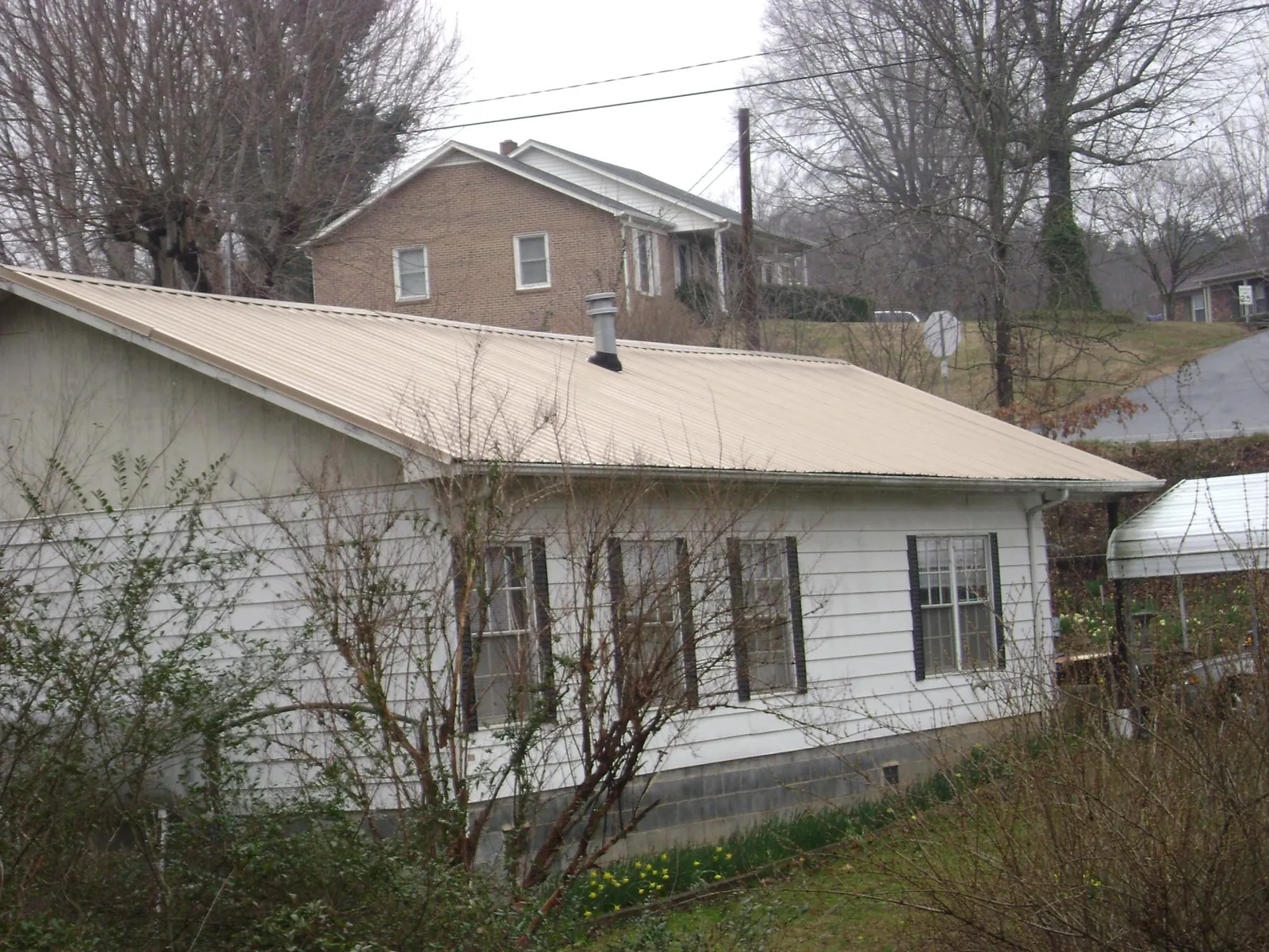Tan metal roof on a white sided house set into a hillside — Commercial Roofing by Roofing Brothers in Reed Point